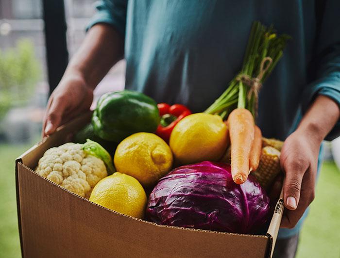 A man holds a carboard box full of fresh produce