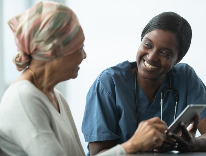 A cancer patient wearing a head scarf talks with a health worker wearing scrubs