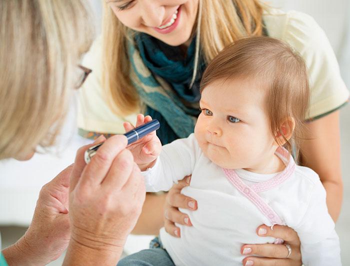 A baby stares at a pen held in front of her by a female physician