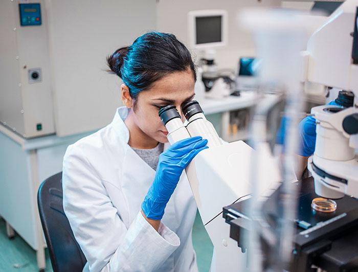 A woman in lab coat peers into microscope