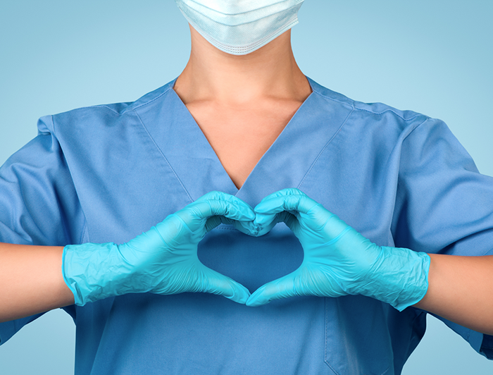 nurse in scrubs makes a heart shape across her chest with her hands