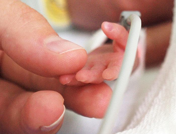 adult hand gently holding the hand of a premature infant