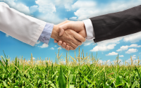 A New Rural Blueprint: Strategic Partnerships That Keep Care Local. A clinician and a businessman shake hands in front of a rural background of a corn field.
