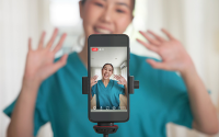 How Health Systems Can Retain Gen Z Workers. A nurse stands in front of a mobile phone that is recording a video of her.