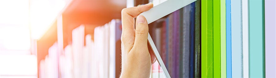 hand pulling an ipad from a shelf full of colorful books